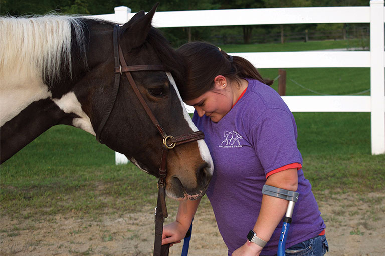 Teen in crutches rubbing heads with a horse