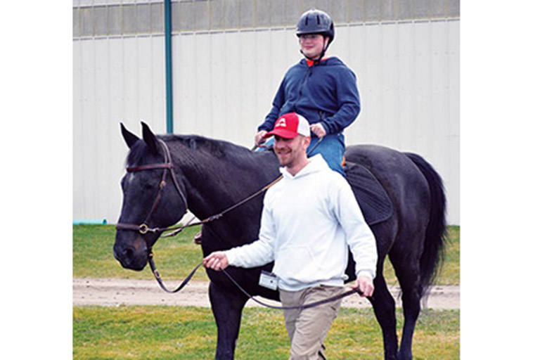 Justin leading a horse with a riding student