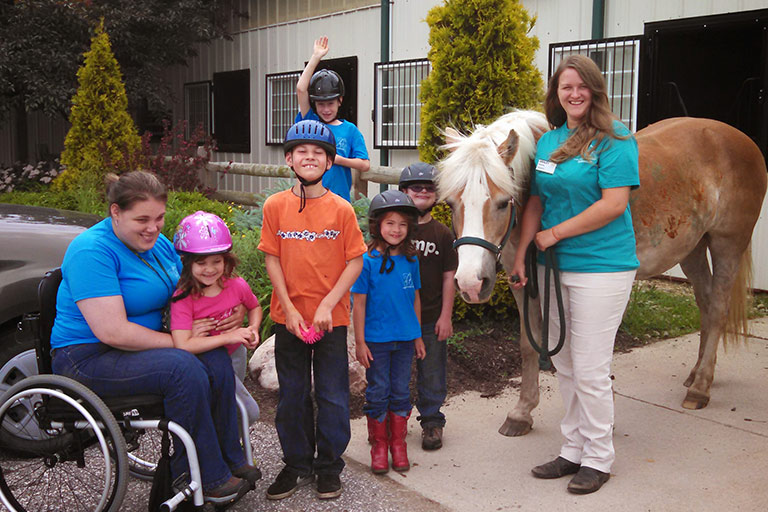 Summer Camp students with a horse in front of the stables